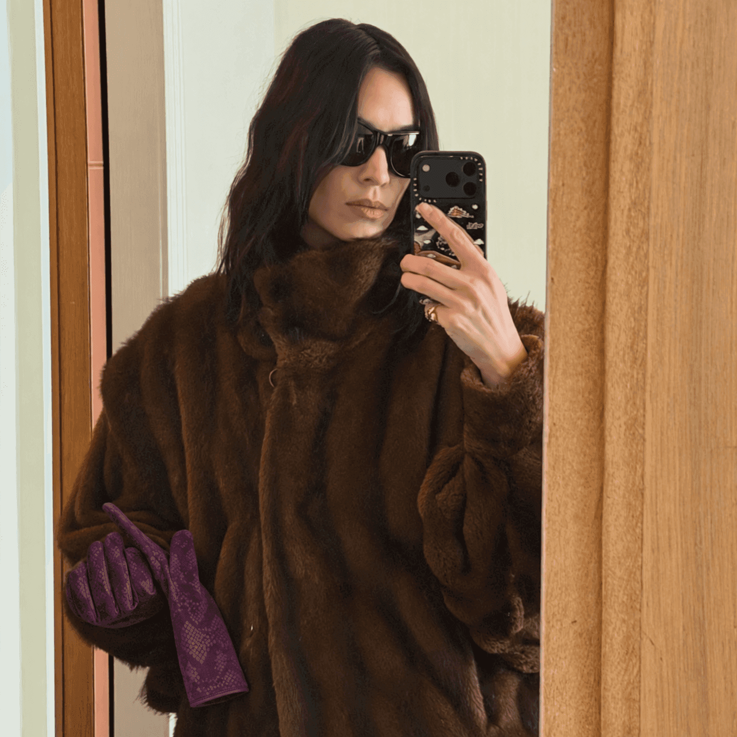 plum python-print suede gloves held against a long chocolate-brown coat in a mirror selfie