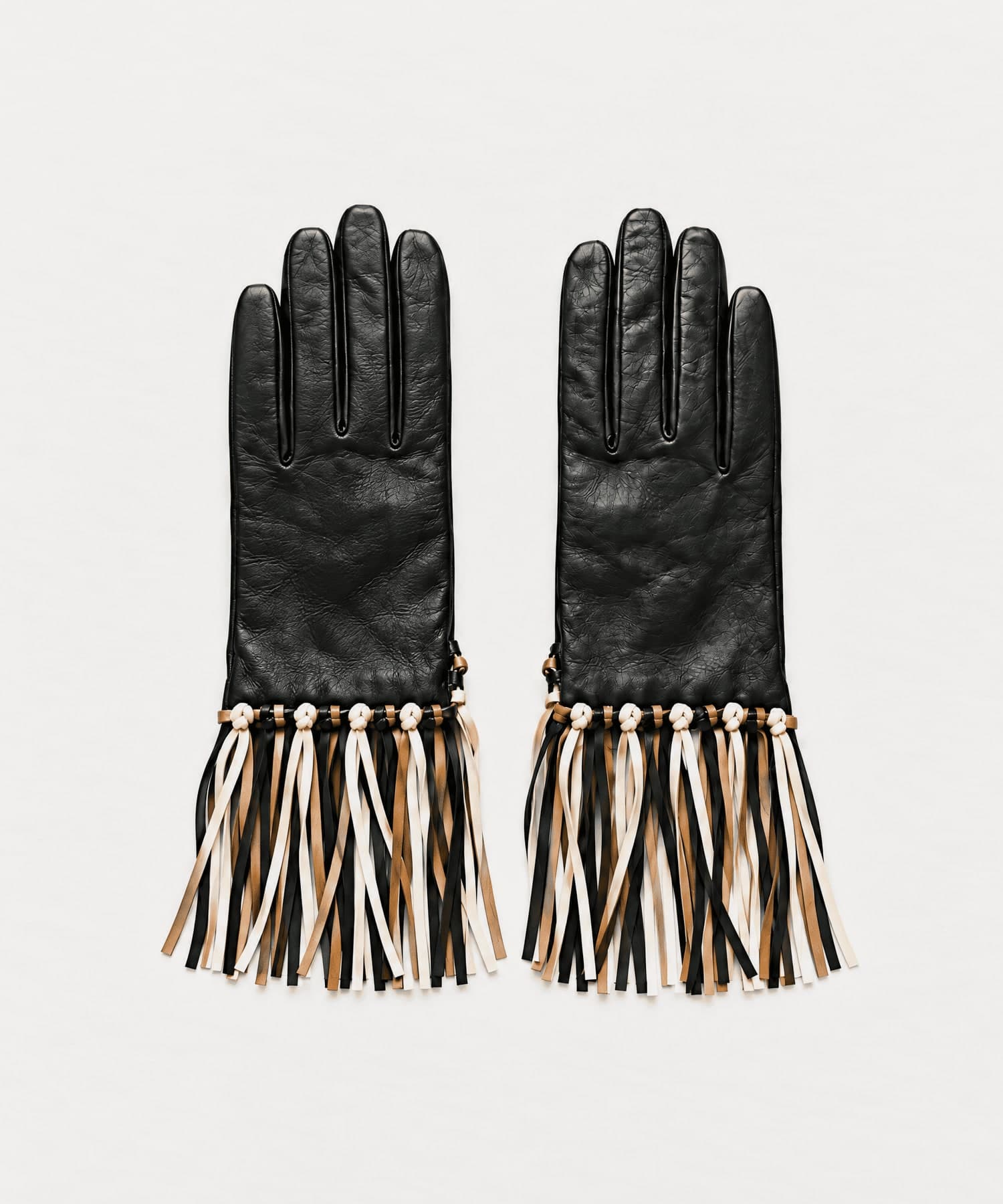 black nappa leather gloves with a black, tan and cream fringe knotted at the wrist, laid flat